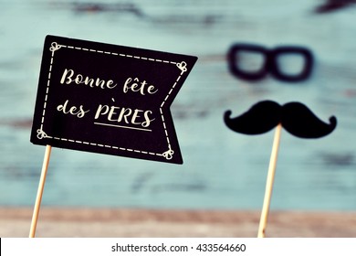 a black flag-shaped signboard with the text text bonne fete des peres, happy fathers day in french, and a mustache and a pair of eyeglasses forming the face of a man, against a blue rustic background