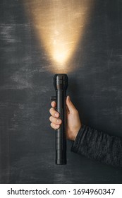 A Black Flashlight In A Man’s Hand And A Ray Of Warm Light In The Dark On A Black Background Pointing Up. Manual Flashlight. Vertical Frame.