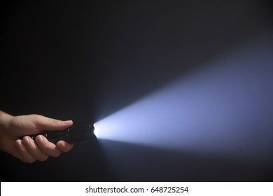 Black flashlight with wide beam in male's hand isolated from left side of the frame on black background