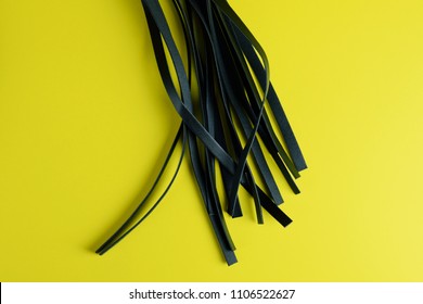 Black flogger whip sex toy for adult, design minimal isolated on yellow background