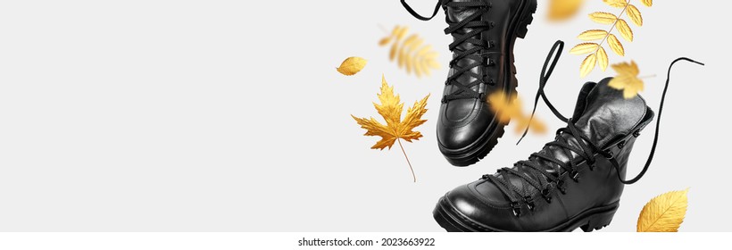 Black flying leather men's or women's boots, autumn golden leaves on light background. Creative concept of autumn shoes. Fashionable stylish hiker boots. Minimalistic footwear Mock up. Unisex boots