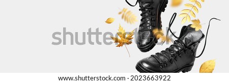Black flying leather men's or women's boots, autumn golden leaves on light background. Creative concept of autumn shoes. Fashionable stylish hiker boots. Minimalistic footwear Mock up. Unisex boots