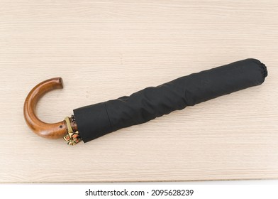 black foldable umbrella with solid wood handle on a wooden surface with copy space