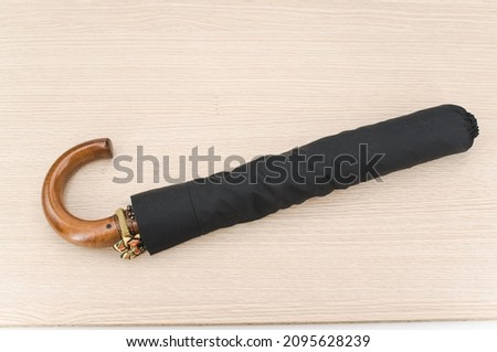 black foldable umbrella with solid wood handle on a wooden surface with copy space