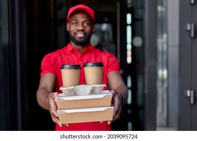 Black Food Delivery Courier Giving Food Boxes And Coffee, Takeaway Male Cafe Worker Outdoors. Concepts Of Ordering Fresh Meals Online, Fast Delivery Service And Using Good Quality Products