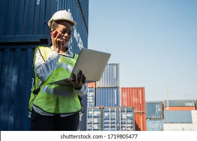 Black foreman woman worker working checking at Container cargo harbor holding laptop computer and walkie-talkie to loading containers. African dock female Logistics import export shipping concept. - Powered by Shutterstock