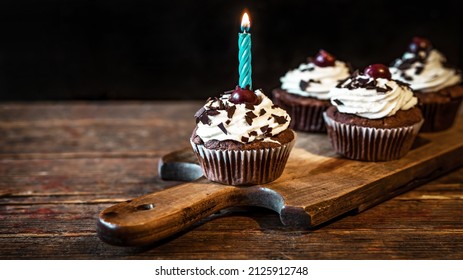 Black Forest Birthday Background Greeting Card Postcard - Black Forest Cherry Cake Cupcakes Muffins With Candle, On Old Rustic Wooden Board On Wooden Table, With Black Background Wall