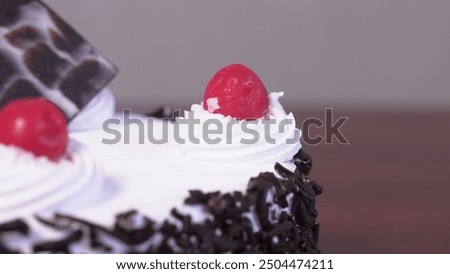 A black forest cake, featuring layers of rich chocolate sponge cake interspersed with whipped cream and tart cherries. Decorated with chocolate shavings, additional cherries.