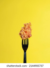 A Black Fork With A Crispy Chicken Nugget Top Of It In The Middle Of A Yellow Background.