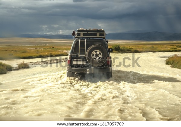 black four by four car crossing a river with splashing\
water, Travel concept for off-road adventure and fun in mountain\
Altai landscape. 