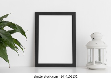 Black Frame Mockup With A Spathiphyllum And Candle Holder On A White Table. Portrait Orientation.