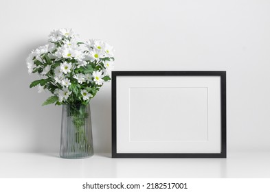 Black Frame Mockup In White Minimalistic Interior With Fresh Flowers Bouquet. Blank Mockup For Artwork, Print Or Photo Presentation.