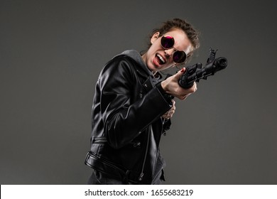 black friday concept. attractive stylish caucasian girl in a black leather jacket and a gray hoody and sunglasses stands with a gun on a dark gray background