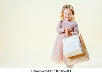 Black Friday. Little Blonde Girl Holds Craft Packages On A Light Solid Background