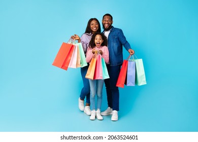 Black Friday Offer Sales And Discounts. Full Body Length Portrait Of Smiling African American Family Holding Paper Bags, Feeling Happy After Successful Shopping, Isolated On Turquoise Blue Studio Wall