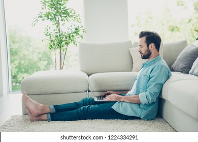 Black Friday online shopping concept. Full legs body size brunet hair man using pc gadget sit on rug floor near comfort couch indoor bright light modern flat in casual jeans denim blue shirt