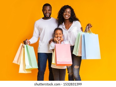 Black Friday. Portrait Of Smiling African American Family With Paper Bags Happy After Successful Shopping, Yellow Studio Background