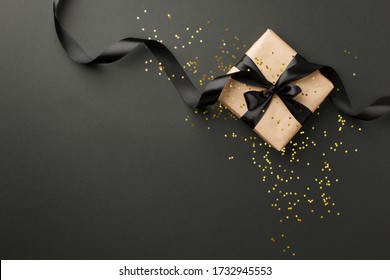 Black Friday sale flat lay with stylish gift box present and ribbon with gold star glitter on black background, flat lay, top view, copy space, xmas and holidays concept
