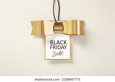 Black friday sale tag with gold bow on beige background