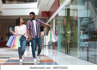 Black Friday Sales. Happy African American Couple Walking With Shopping Bags In Mall, Looking And Pointing At Showcases, Young Spouses Making Purchases Together In Modern Department Store, Copy Space