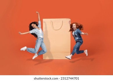 Black friday, season sale, shopping concept. Happy emotional pretty young ladies in stylish casual outfits jumping next to huge shopping bag over orange studio background, mockup, copy space, collage