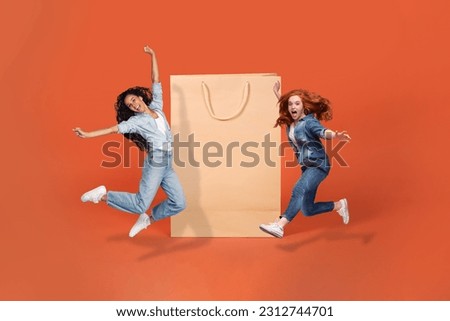 Black friday, season sale, shopping concept. Happy emotional pretty young ladies in stylish casual outfits jumping next to huge shopping bag over orange studio background, mockup, copy space, collage