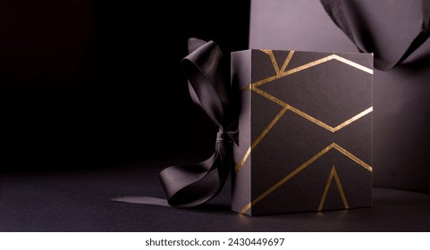 Black Friday Shopping Concept with Black color gift box decorated with Gold Stripes. Gift box Standing against black shopping bag. - Powered by Shutterstock