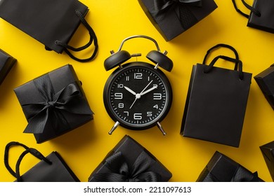 Black friday shopping concept. Top view photo of black alarm clock paper bags and gift boxes with ribbon bows on isolated yellow background - Powered by Shutterstock