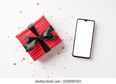 Black friday shopping concept. Top view photo of smartphone red giftbox with ribbon bow and gold sparkle confetti on isolated white background with copyspace