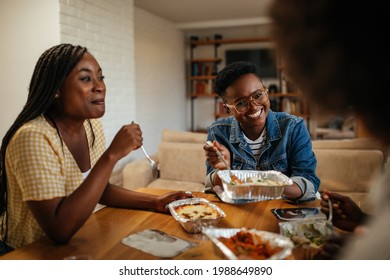 Black friends sitting in the apartment and eating takeaway food.