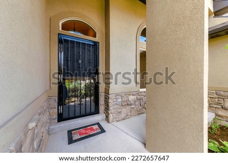Black front door with ornate wrought-iron storm door with glass below. House entrance with transom window near the window on the right.