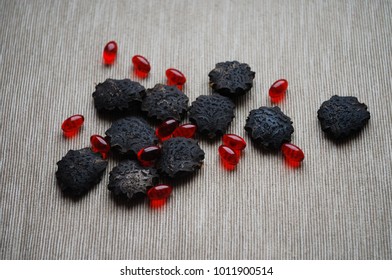 Black gac seeds and oil pills on neutral background.
