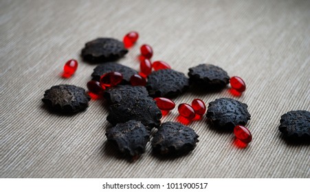 Black gac seeds and oil pills on neutral background.