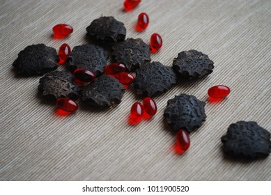 Black gac seeds and oil pills on neutral background.