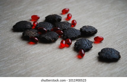 Black gac seeds and oil pills on neutral background.