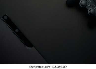 Black game console is flat lay on the black background with controller.