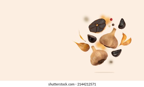 Black garlic bulbs float in the air on a beige background. An image of flying black garlic. Concept of fermented and vegetarian food. Healthy nutrition. Copy space. Horizontal.