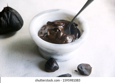 Black garlic creamy aioli paste in white marble bowl with a spoon on the white background
