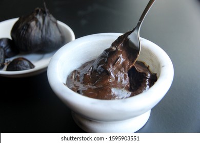 Black garlic creamy aioli in white marble bowl with a spoon on the black background
