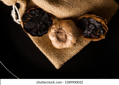 Black garlic on black plate on dark background from above. Culinary food ingredient.