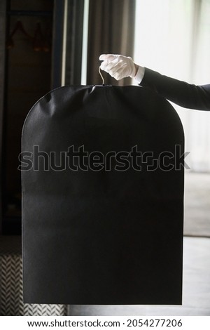 Black garment, suit travel bag. the hands of a hotel worker in white gloves.