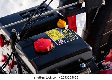 Black Gas Tank Of A Snowblower On A Background Of Snow. Close-up. Black, White, Red. Yellow Safety Instructions.