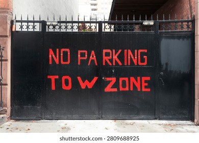 A black gate with red graffiti reading 'NO PARKING TOW ZONE' in an urban setting.
