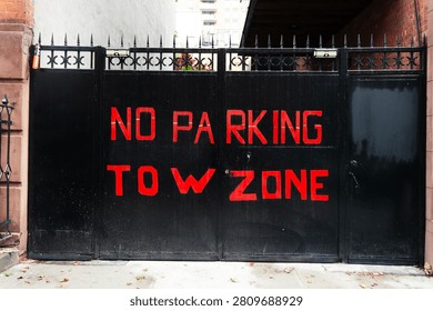 A black gate with red graffiti reading 'NO PARKING TOW ZONE' in an urban setting.
