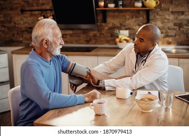 Black General Practitioner Measuring Blood Pressure Of A Senior Man While Visiting Him At Home. 