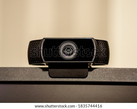 A black generic web camera on top of a screen. With a beige background.