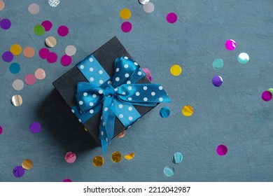 Black Gift Box With Bow And Holiday Tinsel Flat Lay On Dark Cement Background. Top View.