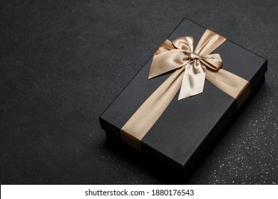 Black gift box with a golden ribbon and a large bow on a granite dark background. Place for the inscription