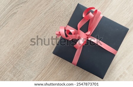 Black gift box on a background, decorated with a textured bow and feathers, creating a romantic atmosphere. Typically used for birthday, anniversary presents, gift cards, post cards.