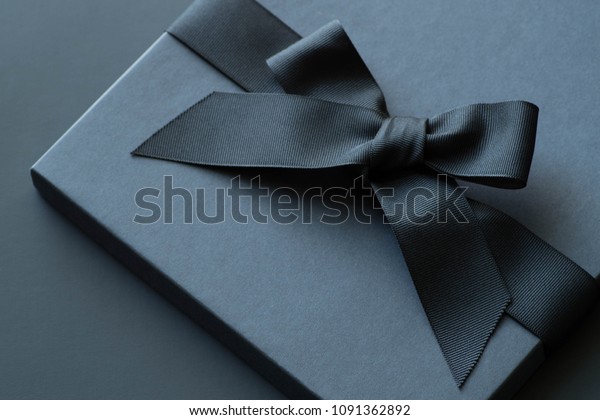 Black gift box on a dark contrasted background,\
decorated with a textured bow and feathers, creating a romantic\
atmosphere. Typically used for birthday, anniversary presents, gift\
cards, post cards.